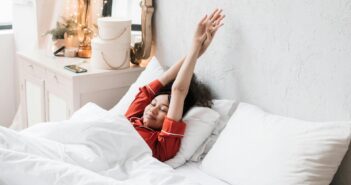 Frau in rotem Pyjama, die im Bett liegt und die Arme in die Höhe streckt.