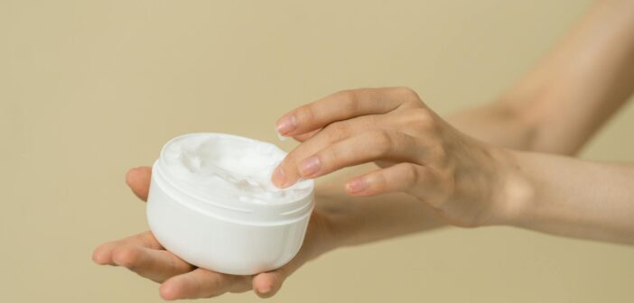 Hände, die einen Cremetiegel halten und mit den Fingern in die Creme eintauchen